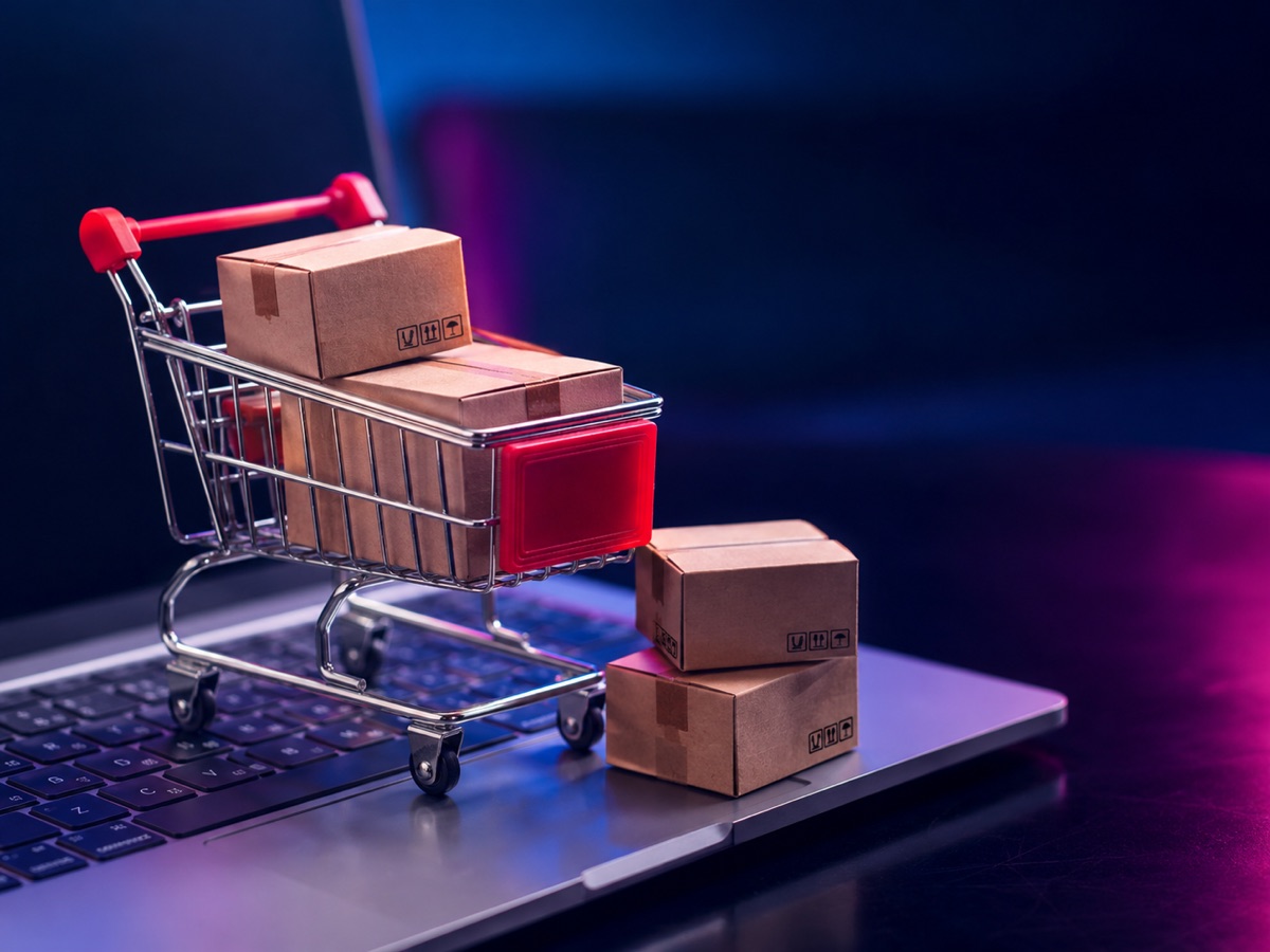 Carrito de compras con cajas sobre una laptop, ilustrando ecommerce y compras en línea